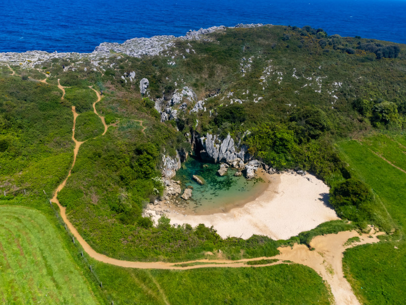 Luftaufnahme der Playa Gulpiyuri mit kleiner Lagune, Sandstrand und Felsen in grüner Küstenlandschaft