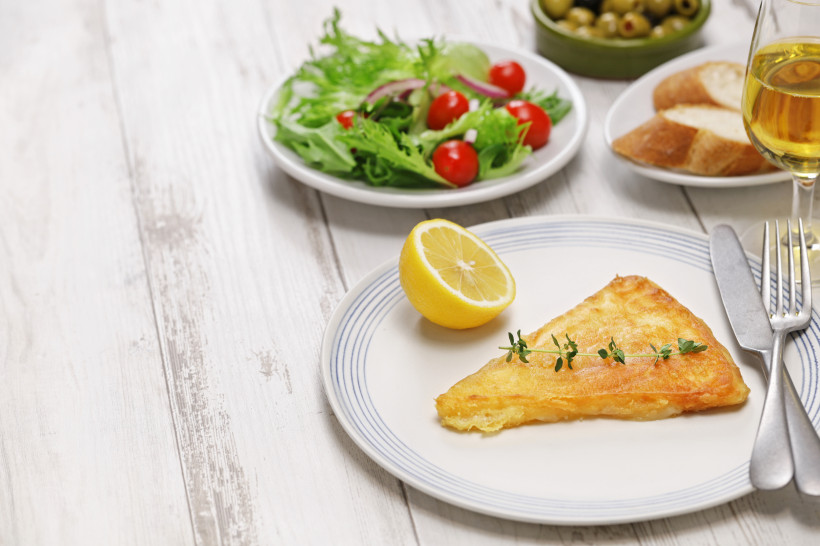 Gebratener Saganaki-Käse auf Teller mit halber Zitrone, dazu Salat und Brot