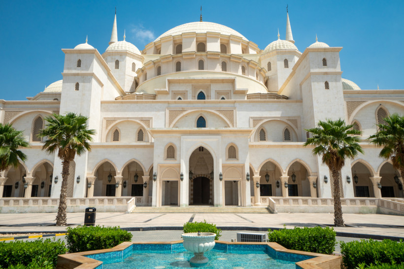 Frontansicht der Scheich-Zayid-Moschee in Fujairah, Vereinigte Arabische Emirate. Prunkvolle weiße Kuppeln, Palmen und Springbrunnen – eindrucksvolle Sehenswürdigkeit.