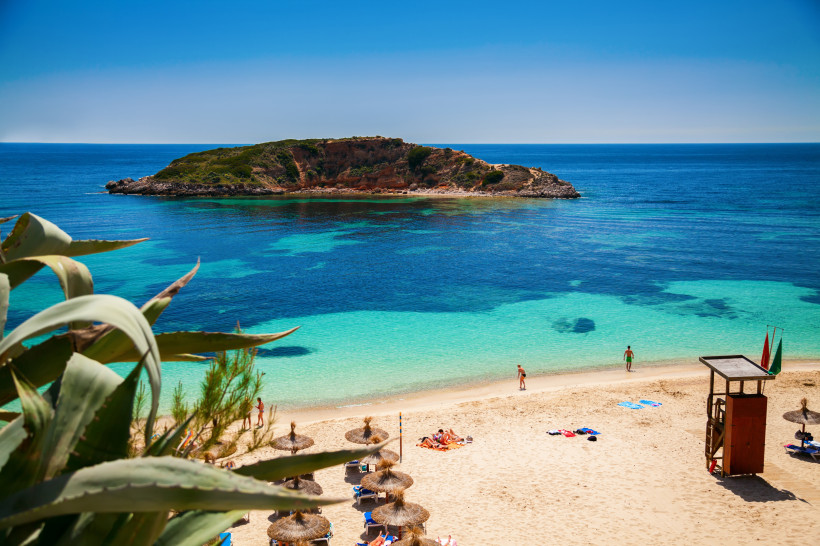 Blick auf den Strand Platja de l’Oratori mit türkisfarbenem Meer und vorgelagerter Insel