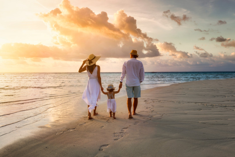 Fujairah, Familienferien  Familie spaziert bei Sonnenuntergang barfuß am Strand entlang, mit Blick aufs Meer.