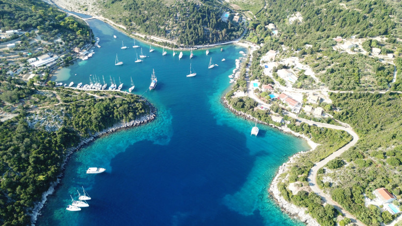 Drohnenaufnahme einer ruhigen Bucht mit Segelbooten und Yachten, umgeben von grüner Natur und Küstendörfern am türkisfarbenen Meer