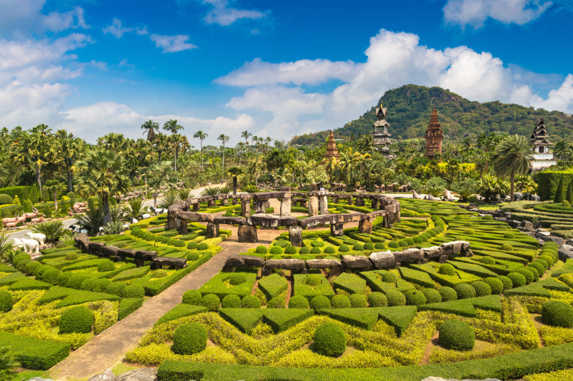Exotischer Landschaftsgarten mit Steinmonument und tropischer Vegetation in Thailand Steinmonument inmitten eines tropischen Landschaftsgartens mit grünen Hecken und Palmen im Nong Nooch Tropical Garden in Thailand