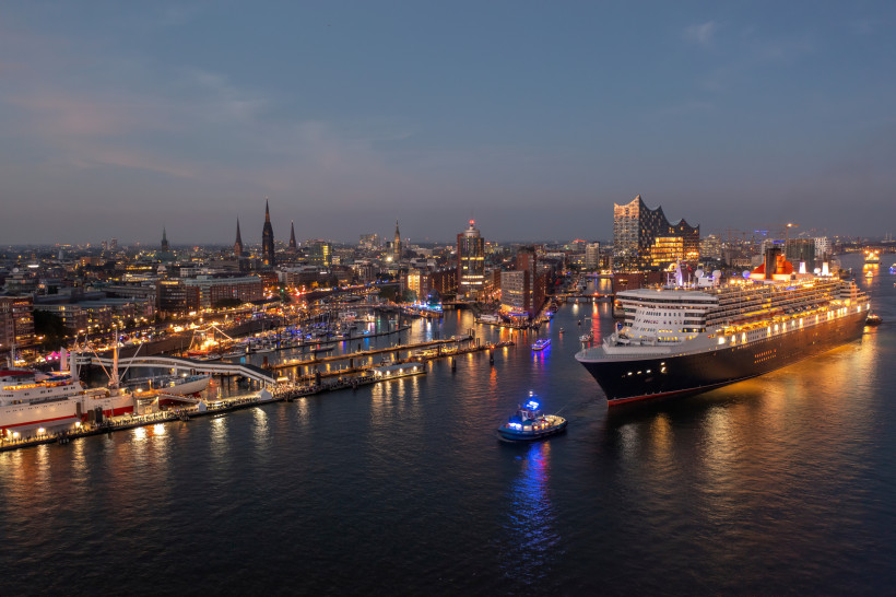 Kreuzfahrten ab Hamburg: Kreuzfahrtschiff im Hafen bei Abenddämmerung Kreuzfahrtschiff im Hamburger Hafen am Abend mit beleuchteter Skyline