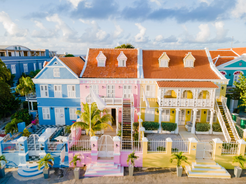 Curaçao Reihe farbenfroher Kolonialhäuser in Willemstad auf Curaçao. Die Gebäude sind in leuchtendem Blau, Rosa und Gelb gestrichen und haben rote Ziegeldächer. Die Architektur ist typisch niederländisch-karibisch, mit Balkonen und weißen Fensterläden