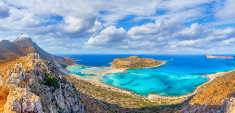 Panoramablick auf die Balos-Lagune mit türkisblauem Wasser, Sandbank und kleiner Insel unter wolkigem Himmel