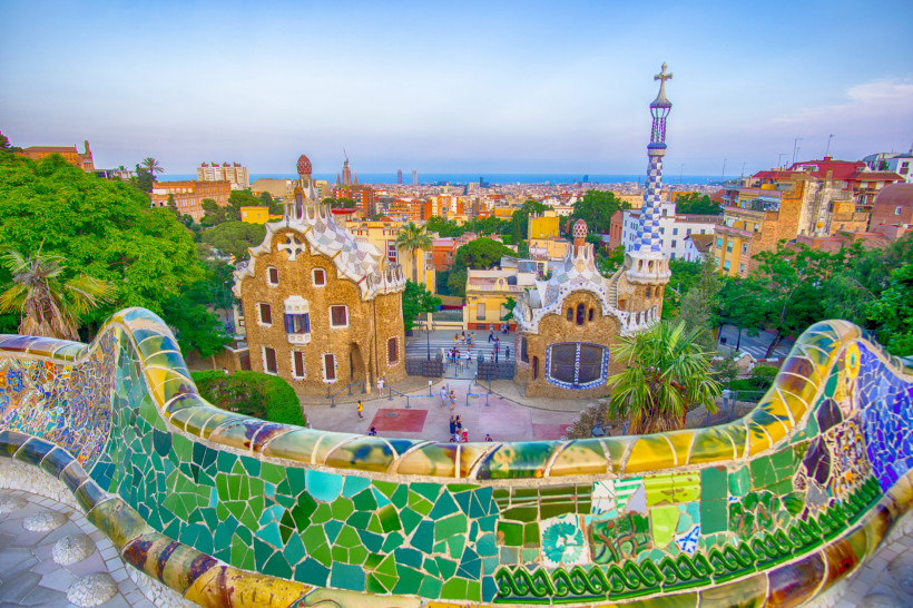 Blick über Park Güell in Barcelona mit Mosaikbank im Vordergrund und den Gebäuden am Haupteingang