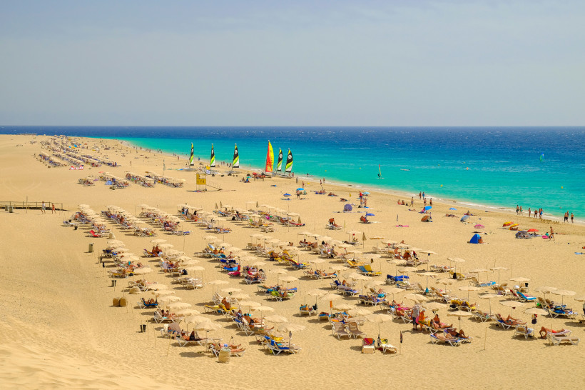 Strand von Morro Jable mit Liegen, Sonnenschirmen und Wassersportsegeln am türkisfarbenen Meer