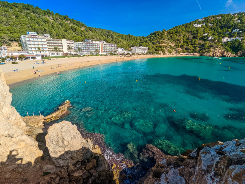 Bucht Cala de San Vicente auf Ibiza mit Sandstrand, türkisblauem Wasser, Hotels und bewaldeten Hügeln
