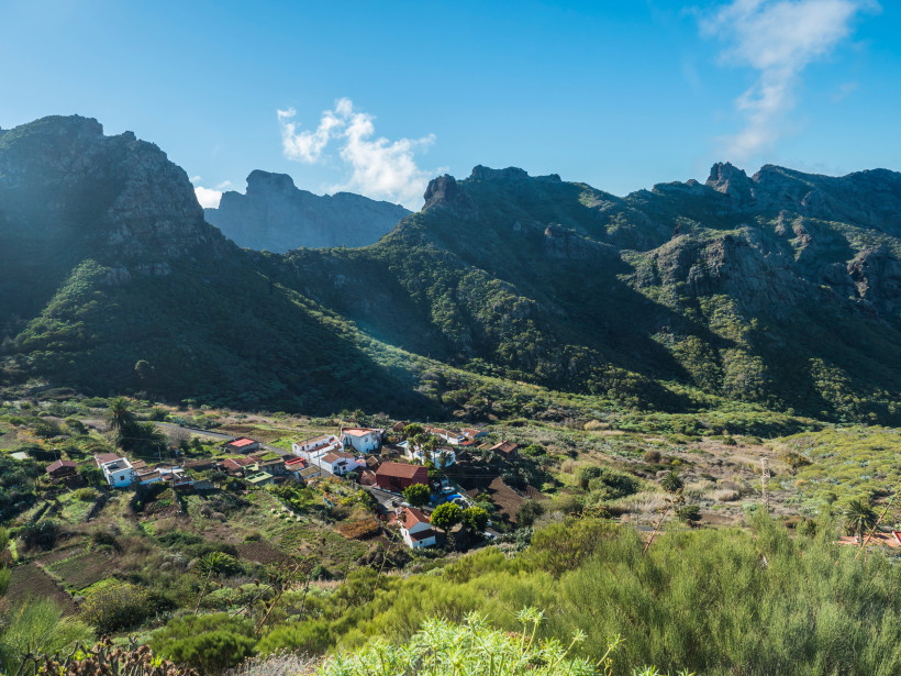 Abgelegenes Bergdorf auf Teneriffa im grünen Tal Kleines Dorf im grünen Bergtal mit Gärten und schroffen Felsformationen im Hintergrund auf Teneriffa