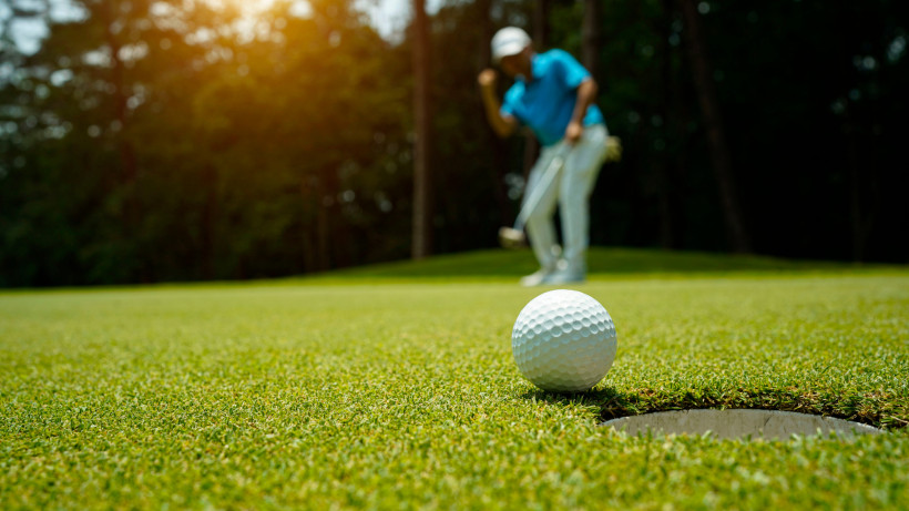 Fujairah, Aktivferien Golfball kurz vor dem Einlochen, mit Golfer im Hintergrund, der seinen Schlag beobachtet