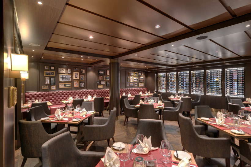 MSC Grandiosa: Spezialitätenrestaurant Butcher’s Cut, Gastraum mit Sitzbereich und Weinregalen Innenansicht des Spezialitätenrestaurants Butcher’s Cut auf der MSC Grandiosa mit gedeckten Tischen und Weinregalen