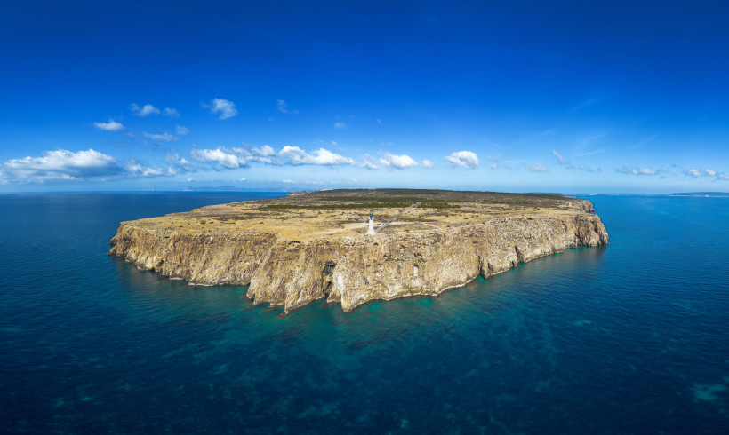 Steilklippen am Cap de Barbaria auf Formentera mit dem weißen Leuchtturm in der Mitte. Weite, karge Landschaft über dem türkisblauen Mittelmeer.