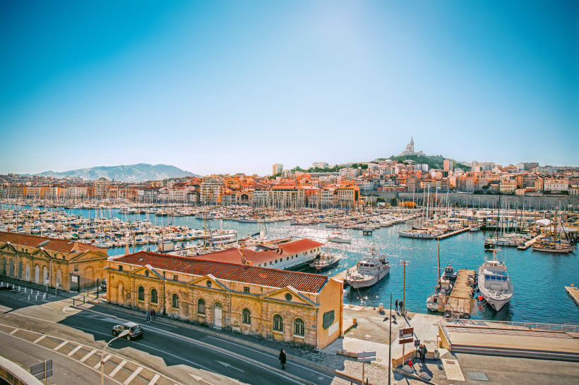 Marseille Vieux-Port von Marseille mit vielen Segelbooten, terrakottafarbenen Häusern und der Basilika Notre-Dame de la Garde auf dem Hügel unter klarem Himmel.