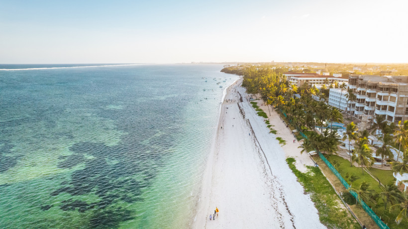 Kenia Luftaufnahme vom Diani Beach an der Südküste Kenias mit weißem Sandstrand, türkisfarbenem Wasser und Palmen. Rechts im Bild Hotels, links das ruhige Meer. Die Szene ist in weiches Abendlicht getaucht