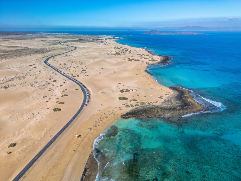 Fuerteventura: Corralejo Dünen und Atlantikküste aus der Luft Luftaufnahme der endlosen Dünenlandschaft von Corralejo mit Straße entlang des Atlantiks und türkisfarbenem Wasser auf Fuerteventura
