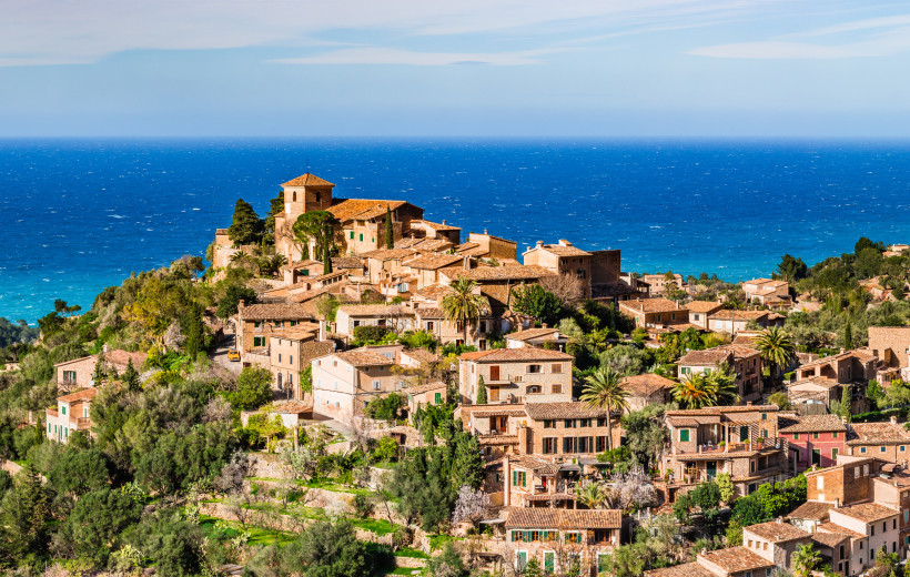 Blick auf das Tramuntana-Dorf Deià mit Natursteinhäusern am Hang und Meer im Hintergrund