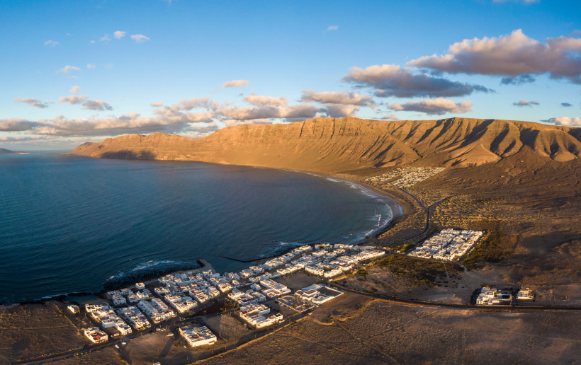 Lanzarote - Famara Luftaufnahme von Famara auf Lanzarote mit weißem Dorf, weitem Strand und imposanten Klippen im Hintergrund.
