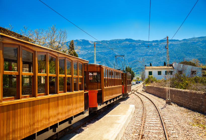 Historischer Holzzug Tren de Sóller auf Gleisen vor Bergkulisse auf Mallorca