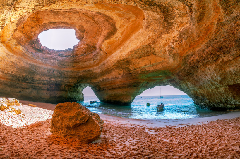 Blick aus der Benagil-Höhle auf Sandstrand und Meer mit Booten, Algarve, Portugal