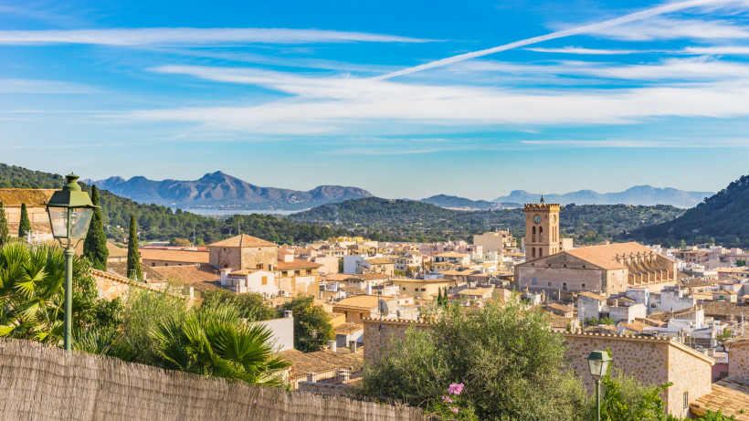 Panoramablick über die Dächer von Pollença mit der Pfarrkirche Nostra Senyora dels Àngels und den Bergen der Serra de Tramuntana im Hintergrund.