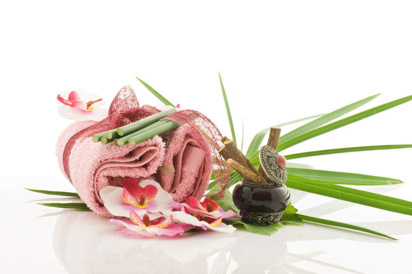 Ägypten - Marsa Alam Wellness-Arrangement mit rosa Handtuch, Blumen, Palmblättern, Bambusstäben und einem kleinen Gefäß mit Zimtstangen und orientalischem Deckel. Der Hintergrund ist weiß.