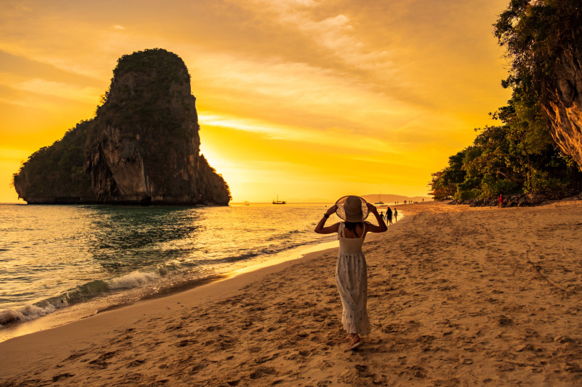 Thailand Sonnenuntergang am Strand – Frau spaziert an Felskulisse in Krabi Frau spaziert bei Sonnenuntergang am goldenen Strand von Krabi mit markanter Felskulisse – ideal für Thailand Reisen und verschiedene Reisetypen.