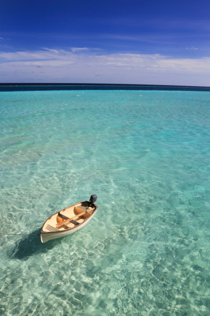 Kleines Boot treibt im klaren, türkisfarbenen Wasser der Malediven
