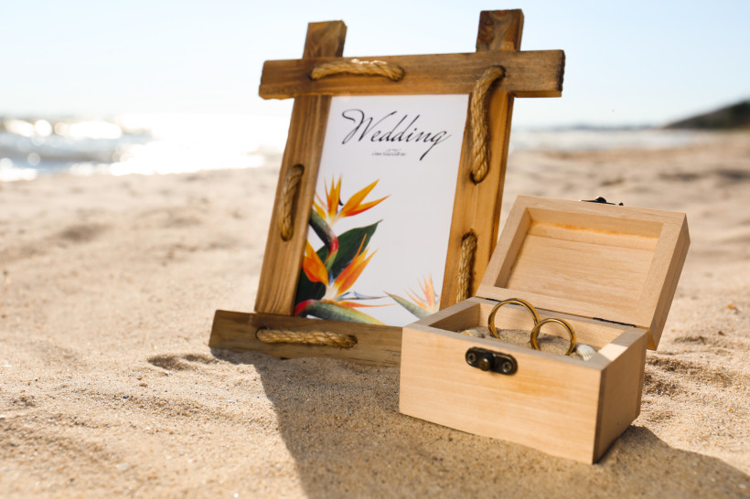 Hochzeit am Strand von Lanzarote – Trauringe Holzbox mit Trauringen und Hochzeitseinladung im Bilderrahmen am Strand von Lanzarote – symbolische Szene für eine romantische Hochzeitsreise oder Strandhochzeit.