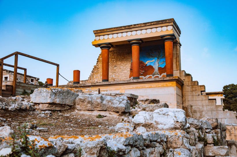 Palast von Knossos: rekonstruierter Gebäudeteil mit roten Säulen und Fresko Rekonstruktion im Palast von Knossos mit roten Säulen und Wandmalerei vor blauem Himmel