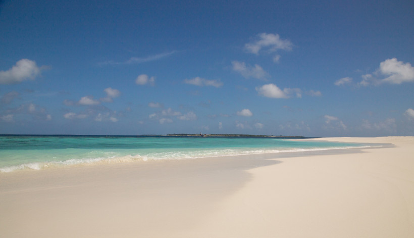 Weißer Sandstrand an einem Atoll auf den Malediven mit türkisfarbenem Meer und blauem Himmel