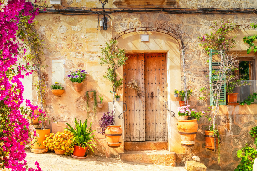 Valldemossa, Mallorca Rustikale Holztür eines traditionellen mallorquinischen Hauses, umgeben von Blumentöpfen und mediterraner Dekoration