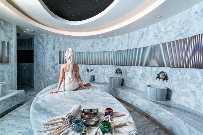 Türkei Frau in Handtuch und Turban sitzt entspannt im luxuriösen Marmor-Hamam mit orientalischer Dekoration