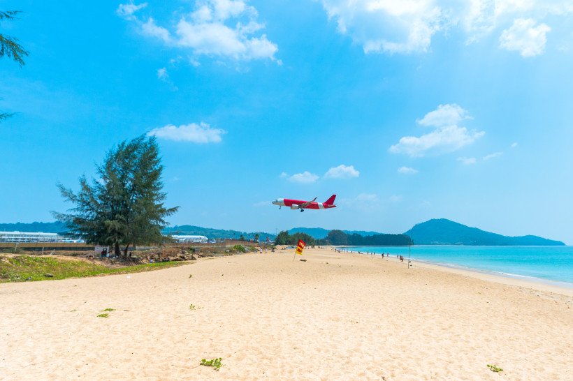 Sandstrand am Mai Khao Beach mit Meer und tief fliegendem Flugzeug am Himmel