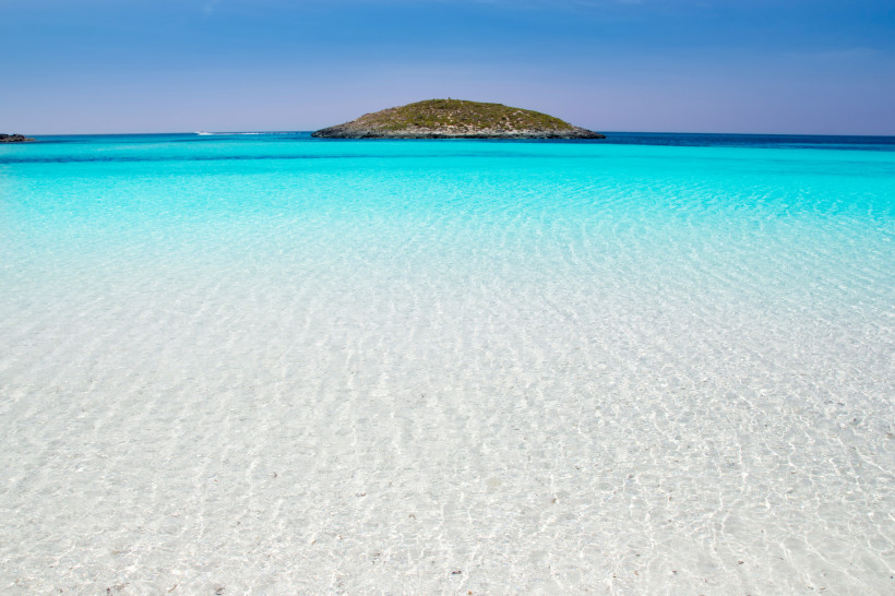 Türkisfarbene, flache Lagune mit Sandboden und kleiner Insel am Horizont vor Formentera