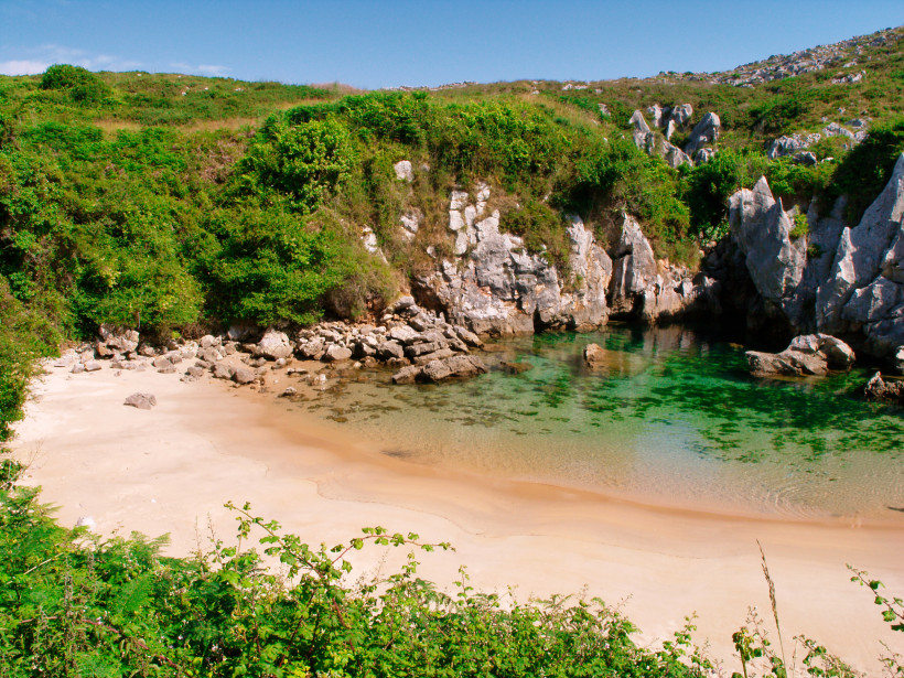 Playa de Gulpiyuri mit kleinem Sandstrand, klarem Wasser und felsiger, bewachsener Küste