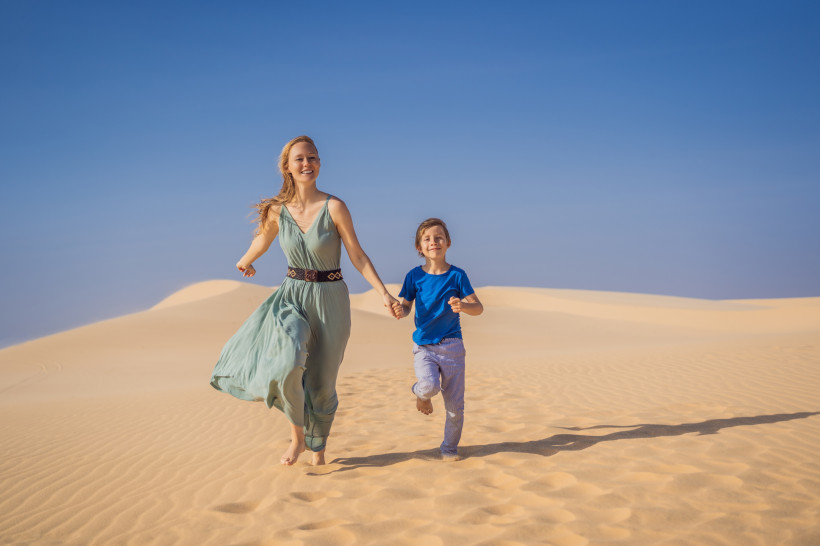 Freiheit in den Dünen von Maspalomas Mutter und Kind laufen barfuß über die goldgelben Sanddünen von Maspalomas auf Gran Canaria. Der strahlend blaue Himmel und die Weite der Landschaft schaffen eine magische Urlaubsatmosphäre.