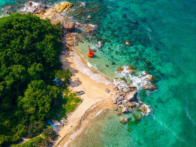 Geheime Bucht mit Felsen, roter Boje und türkisblauem Wasser an einer tropischen Küste Versteckte kleine Bucht mit Sandstrand, grüner Vegetation, Felsen, klaren Wellen und einer roten Boje im türkisblauen Meer