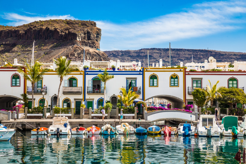 Hafenbecken in Puerto de Mogán mit Booten, weißen Gebäuden und Palmen vor felsiger Küstenlandschaft