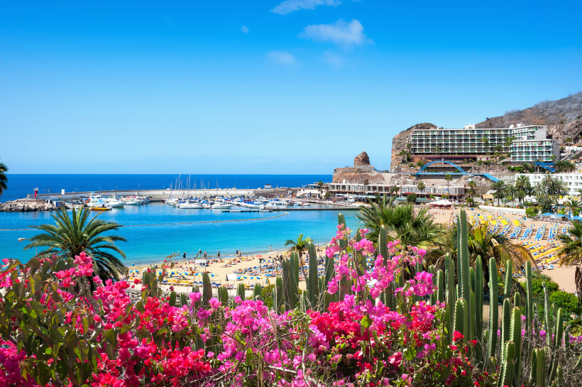 Blick auf Strand und Hafen von Puerto Rico auf Gran Canaria mit Yachten, Hotelanlage und Küstenfelsen