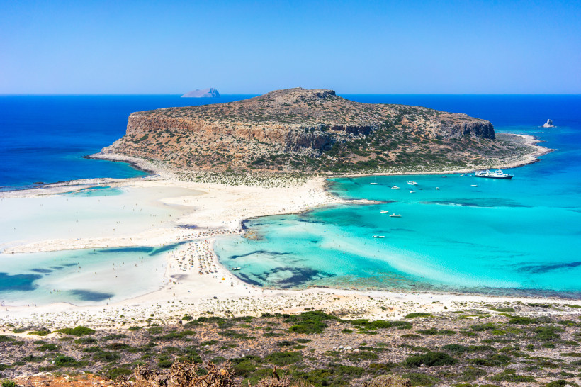 Luftaufnahme einer Lagune mit türkisfarbenem Wasser, Sandstrand und felsiger Halbinsel im Hintergrund