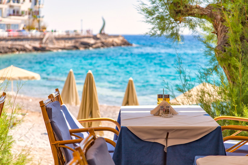 Urlaub für Paare: Strandterrasse mit gedecktem Tisch und Meerblick Gedeckter Tisch auf einer Terrasse am Strand mit Blick auf das Meer und Sonnenschirme