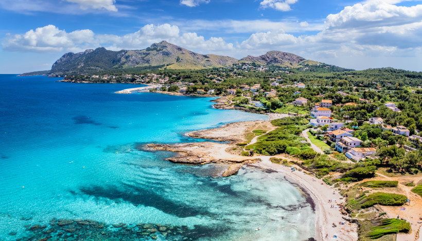 Alcúdia, Mallorca Luftaufnahme der Küste von Nordmallorca mit türkisblauem Meer, Sandstrand, Felsen und Blick auf das Tramuntana-Gebirge bei Alcúdia