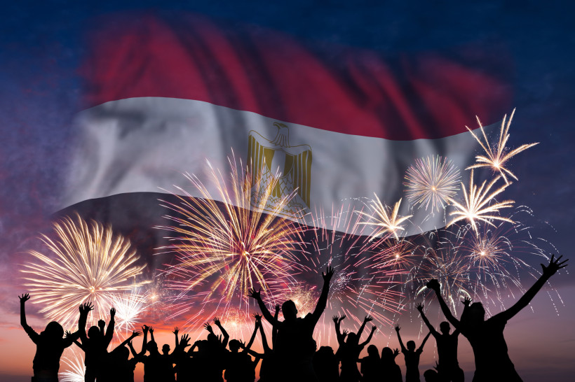 Ägypten - Hurghada Eine Menschenmenge feiert ausgelassen mit erhobenen Armen vor einem Feuerwerk am Abendhimmel. Im Hintergrund ist groß die ägyptische Flagge eingeblendet.