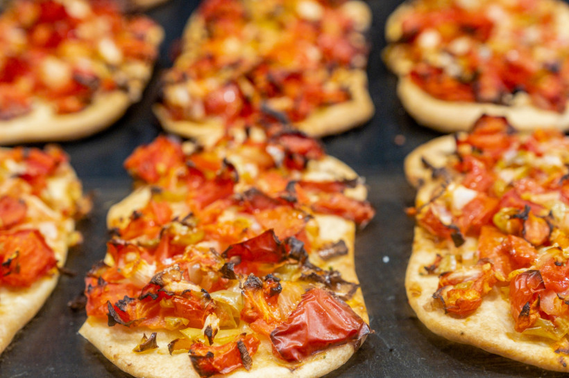 Mallorca Mehrere Portionen einer typischen mallorquinischen Coca – ein herzhaftes Fladenbrot – belegt mit gehackten Tomaten, Zwiebeln und Paprika. Die Zutaten sind leicht angeröstet, der Teig goldbraun gebacken. Die Coca liegt auf einem dunklen Blech und wirkt fri