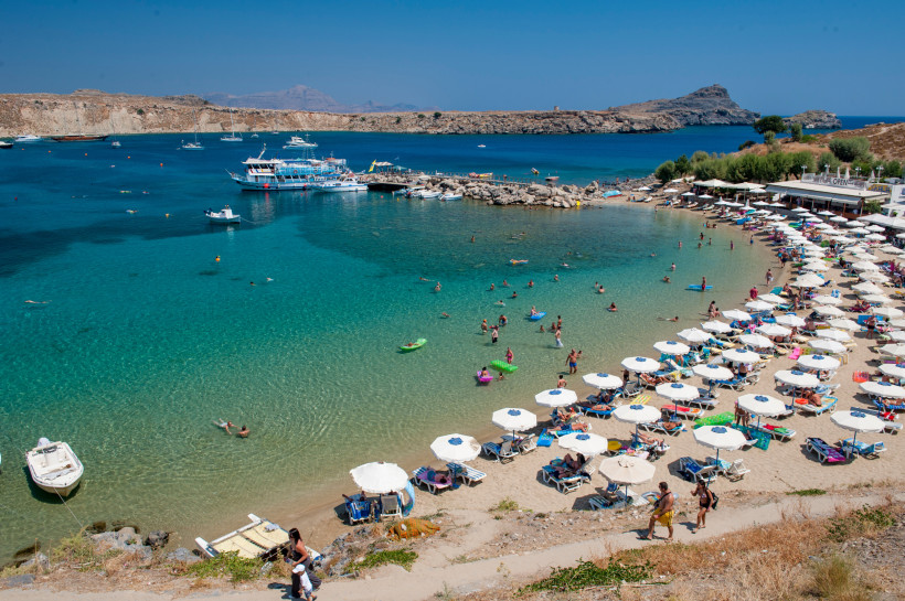 Traumbucht auf Rhodos mit türkisblauem Wasser, Badegästen, Strandliegen und Booten – beliebter Ort für Strandurlaub in Griechenland