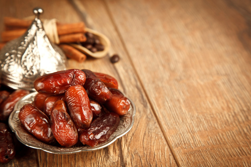 Ras al Khaimah, Ramadan Ein silberner Teller mit frischen Datteln, im Hintergrund Zimtstangen und eine verzierte Metallschale auf einem Holztisch