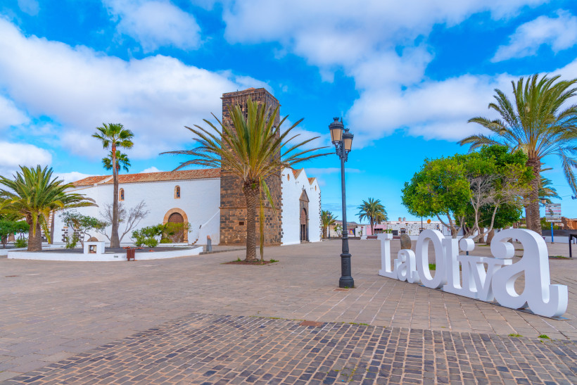 La Oliva Ortszentrum mit Kirche und Palmen – Historisches Herz des Nordens von Fuerteventura Zentrum von La Oliva auf Fuerteventura mit der Iglesia de la Candelaria, Palmen, weiß getünchten Häusern und dem La-Oliva-Schriftzug.