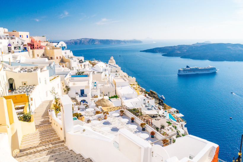 Santorini - Fira (Thira) Fira auf Santorini: weiße Kykladenhäuser und Terrassen über der Caldera, unten ein Kreuzfahrtschiff im tiefblauen Meer