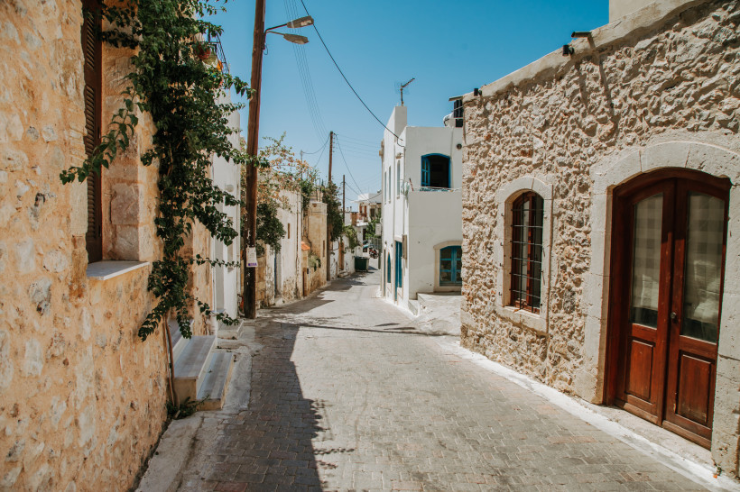 Schmale Gasse im Old Village Malia mit Natursteinfassaden, weißen Häusern und Holztür